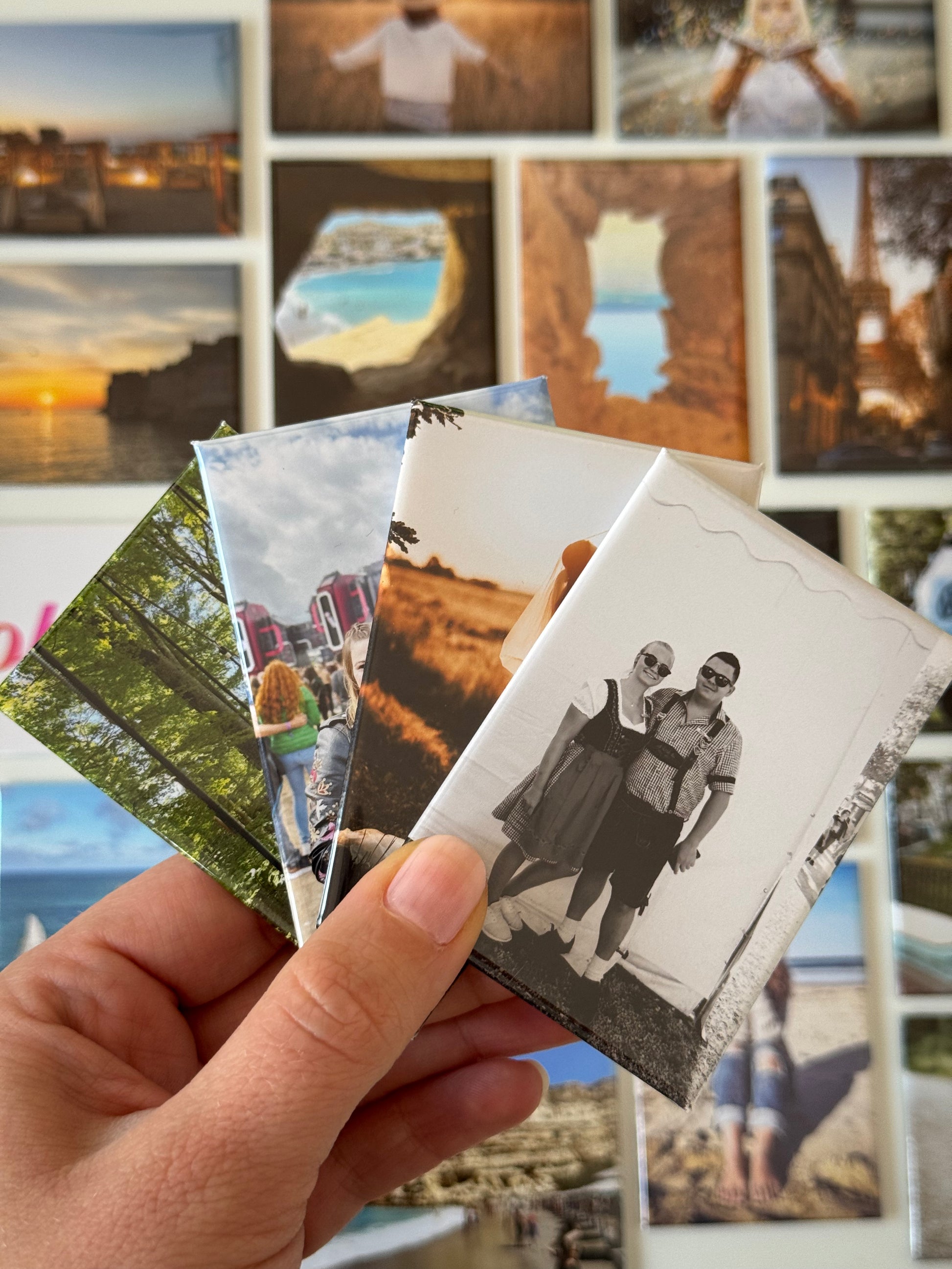 4 Fotomagnete in der Hand. Im Hintergrund mehrere andere Fotomagnete mit verschiedenen Motiven drauf